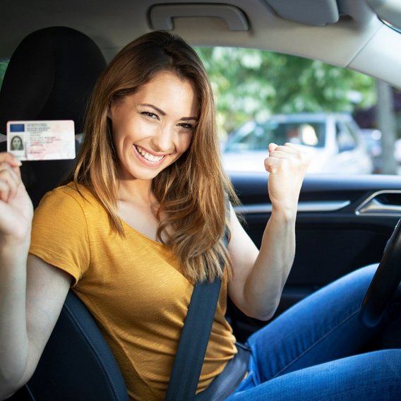 Glückliche Frau im Auto zeigt ihren Führerschein
