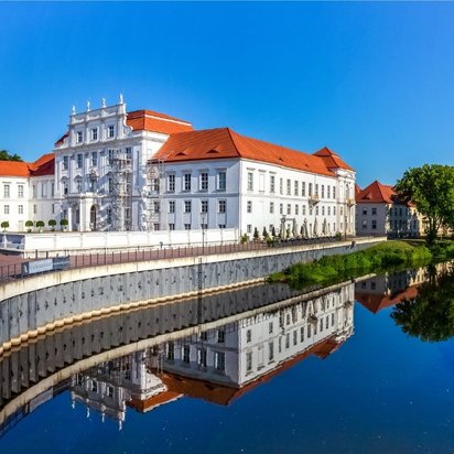 Schloss Oranienburg mit Fluss und Promenade bei sonnigem Wetter