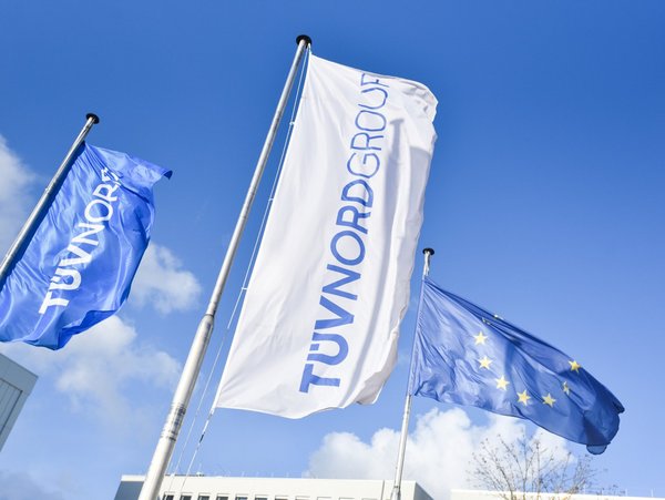 Fahnen der TÜV NORD GROUP und der EU wehen vor blauem Himmel