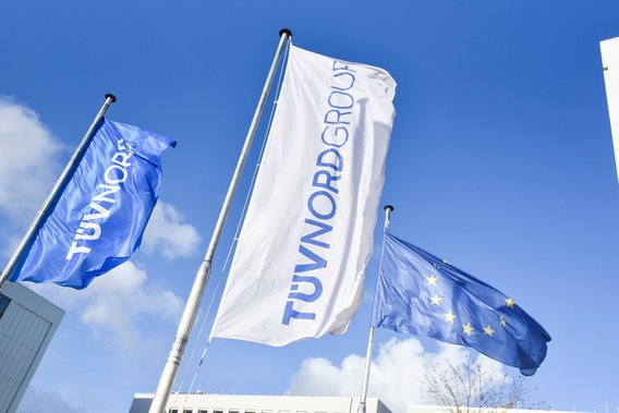Fahnen der TÜV NORD GROUP und der EU wehen vor blauem Himmel