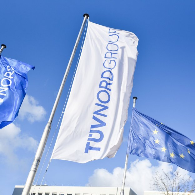 Fahnen der TÜV NORD GROUP und der EU wehen vor blauem Himmel