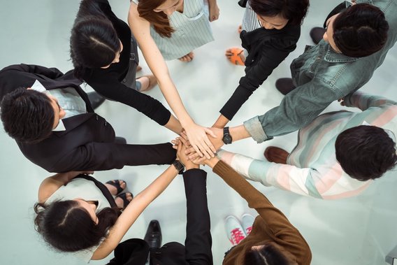 Gruppe von Menschen steht im Kreis und legt gemeinschaftlich die Hände übereinander