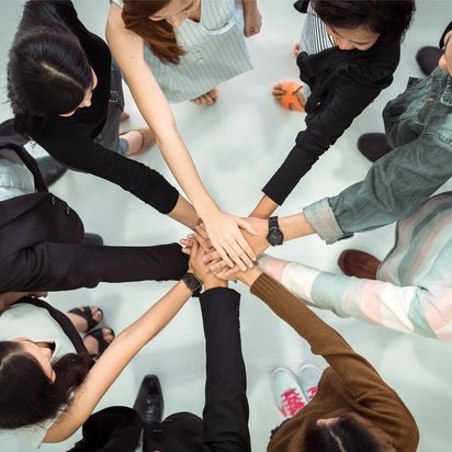 Gruppe von Menschen steht im Kreis und legt gemeinschaftlich die Hände übereinander