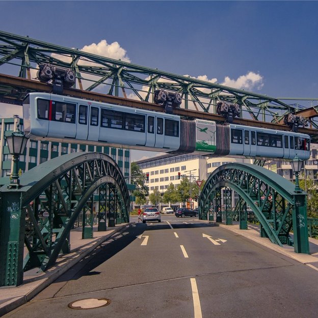 Die Wuppertaler Schwebebahn überquert eine Straße nahe der Station Kluse bei sonnigem Wetter
