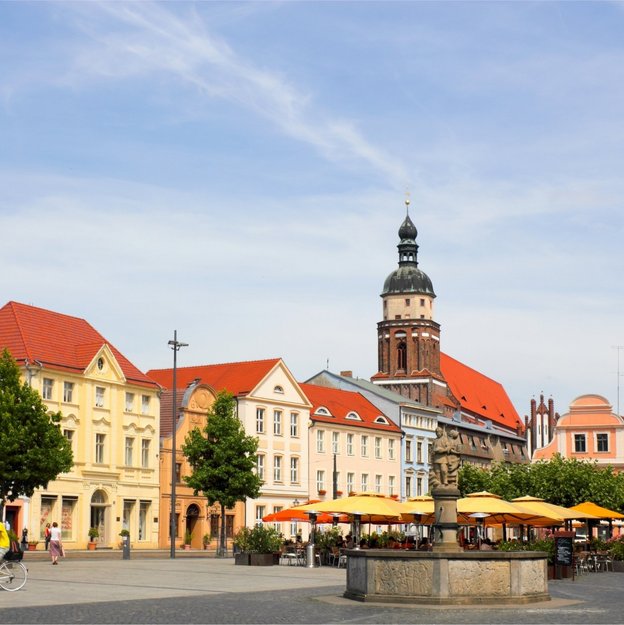 Historischer Marktplatz in Cottbus mit Springbrunnen, bunten Häusern und Kirchturm im Hintergrund
